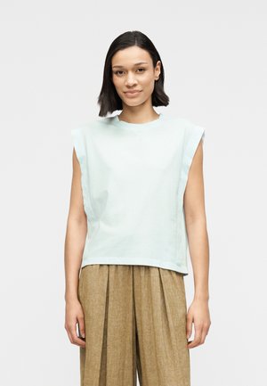 Hellblaues ärmelloses Oberteil aus weichem Stoff, mit lockerer Passform und rundem Ausschnitt, kombiniert mit beigen, plissierten Hose mit weitem Bein.