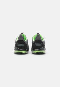 Ett par svarta och grå Puma-sneakers med neongrön insida och genomskinliga luftkuddssulor, visade bakifrån mot en vit bakgrund.