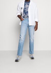 Camisa blanca de gran tamaño, camiseta de teñido anudado azul, jeans rectos de color azul claro y zapatillas grises con acentos de color. Diseño simple y ajuste casual.