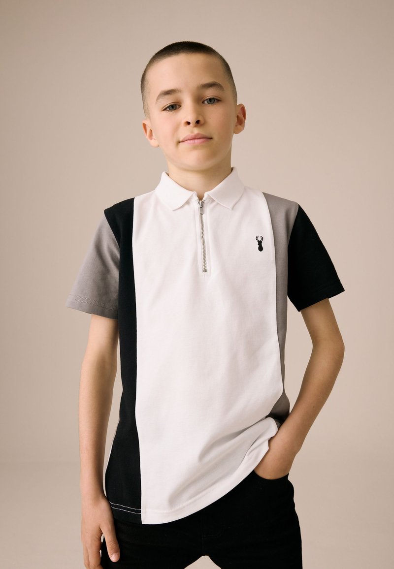 Polo a maniche corte con collo a zip, design a blocchi di colore in nero, bianco e grigio, con un piccolo logo sul petto.