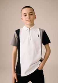 Rövid ujjú galléros póló, cipzáras nyakkal, színblokkolt design fekete, fehér és szürke színekben, kis logóval a mellrészen.