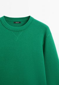 Grøn crewneck-trøje med ribbet krave og V-sømme detalje under halsudskæringen, lavet af strikket stof.