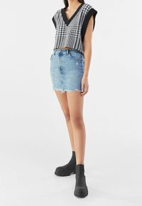 Svart och vit houndstooth stickad topp med korta ärmar, kombinerad med en ljusblå denimminikjol med fransar och slitna detaljer. Svarta anklarstövlar.