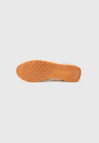 Light-colored sneaker outsole with a textured surface featuring an orange rubber grip and a geometric pattern for traction.