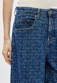 Jeans dżinsowe z niebieskim praniem, z wytłoczonym powtarzającym się wzorem logo "Tommy Jeans", pięć kieszeni oraz standardowe zapięcie na metalowy guzik.