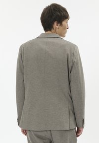 Sacou gri cu un material texturat, fante unice la spate, rever fasonat și manșete cu nasturi. Croială ajustată cu linii curate.