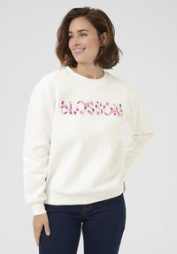 Crewneck sweatshirt in off-white with pink floral embroidery across the chest. Features long sleeves and ribbed cuffs. Soft fabric texture.
