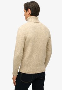 Suéter de punto beige con cuello alto, con dobladillo y puños acanalados, que presenta una textura suave y un corte holgado para mayor comodidad.