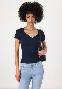 Marin V-hals T-skjorte i bomull, slim fit. Har korte ermer og en liten logo på brystet. Båret med lyseblå jeans og en svart veske.