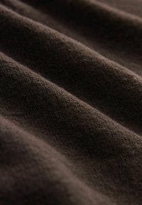 Brauner Stoff mit einer weichen Textur, der sichtbare Rillen und verschiedene Schattierungen aufweist, die Tiefe und ein reichhaltiges Aussehen erzeugen.