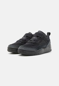 Chaussures de sport noires avec un mélange de matériaux en daim et en maille, présentant des sangles, des lacets, des accents texturés et une semelle en caoutchouc.