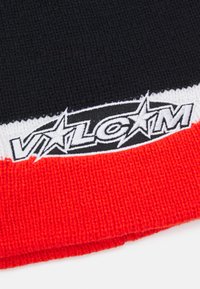 Červená, černá a bílá pletařská čepice s výrazným vyšitým logem a hvězdami. Měkká textura a pruhovaný vzor na okraji.