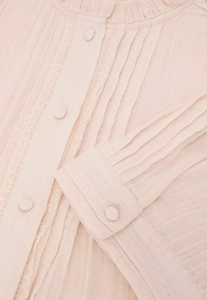 Mīksta rozā blūze ar auduma pārklātiem pogām, vertikālām krokām, mežģīņu apdari gar pogu rindu un krokotu aproču detaļu garo piedurkņu galā.