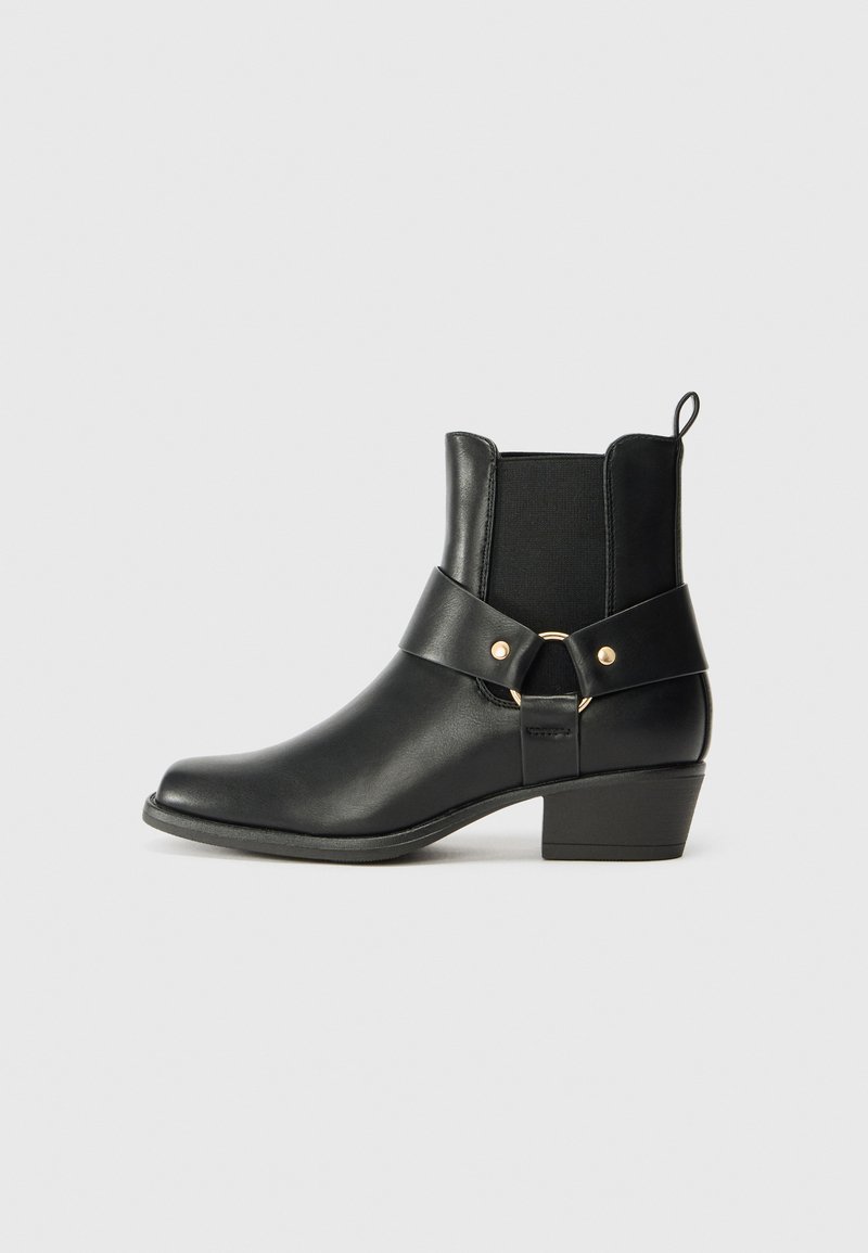 Sorte lær ankle boot med rund tå, elastiske sidepaneler og en dekorativ rem med en guldring som accent. Klossålsdesign.