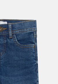 Τζιν παντελόνι σε σκούρο μπλε χρώμα, με μπροστινές τσέπες, ορατές ραφές και μεταλλικό κουμπί κλεισίματος στη μέση.