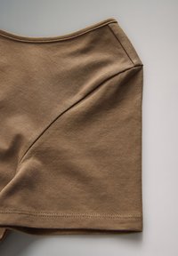 Pruun puuvillane top, millel on sile tekstuur, ümarrandne kaelus ja esiküljel diagonaalne õmblusetdetail. Alläärel on nähtav õmblus.