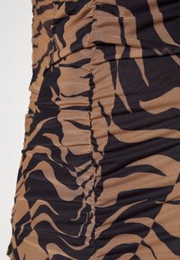 Vêtement en tissu froncé avec un motif rayé tigre noir et beige, présentant des sections froncées et une texture lisse.