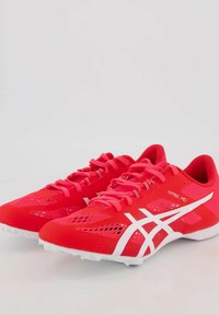 Scarpe da ginnastica rosse con parte superiore in rete, dettagli bianchi e lacci. Presentano un design leggero e una suola stampata con speroni per una maggiore aderenza.