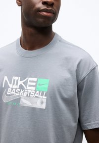 Κοντινό πλάνο ενός ατόμου που φοράει γκρι μπλουζάκι μπάσκετ Nike με λευκό και πράσινο λογότυπο και κείμενο που λέει "Just Do It."