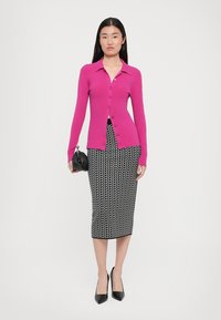 Fuchsia Hemdbluse mit langen Ärmeln, kombiniert mit einem figurbetonten Rock in schwarz-weißer geometrischer Musterung und schwarzen High Heels.