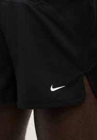 Μαύρο αθλητικό σορτς με λευκό λογότυπο Nike, φορεμένο από ένα άτομο, με υφή υφάσματος και λεπτομέρεια πλευρικής σχισμής.