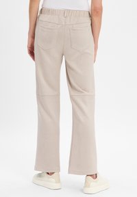 Helle beige, weite Hosen mit elastischem Bund und hinteren Taschen, aus einem weichen, glatten Stoff, mit dezenten Nahtdetails.