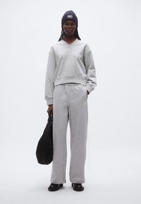 Harmaa V-kaula-aukollinen collegepaita, jossa on resorireunus, yhdistettynä samanvärisiin harmaisiin collegehousuihin ja mustaan laukkuun. Malli käyttää tummansinistä pipoa.