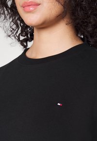 Sudadera negra con cuello redondo y puños acanalados, que presenta un pequeño logo bordado en rojo, blanco y azul en el pecho.