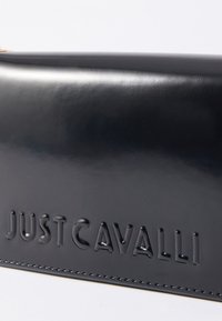 Modra, sijajna usnjena torba z odtisnjenim logotipom "JUSTCAVALLI", gladko teksturo in kontrastnim �šivom ob robovih. Pravokotna oblika.