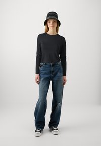 Svart langermet topp, avslappede blå jeans med slitte detaljer, og svart bøttehatt. Hvite joggesko med svarte lisser fullfører stilen.