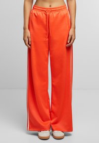 Weite Sweatpants in leuchtendem Orange mit weißen Seitenstreifen, ausgestattet mit einem elastischen Taillenbund und Kordelzug für eine verstellbare Passform.