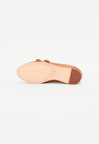 Suola di scarpa in pelle marrone con doppia fibbia, accento in gomma vicino alla punta, finitura liscia e nome del marchio impresso; soletta interna morbida beige.