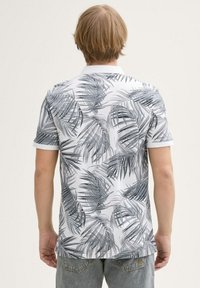 Koszula polo z krótkim rękawem o białej bazie, z czarnym i szarym nadrukiem liści palmowych oraz białą kołnierzykiem. Widok z tyłu wyraźnie pokazuje wzór.