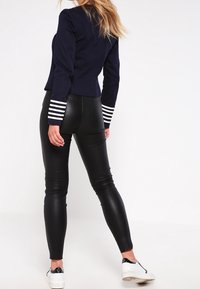 Granatowa krótka marynarka z białymi paskowanymi mankietami, połączona z czarnymi dopasowanymi legginsami i białymi tenisówkami. Gładka tekstura i dopasowany krój.