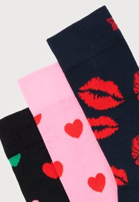 Τρία ζευγάρια κάλτσες σε μαύρο, ροζ και ναυτικό μπλε με κόκκινα σχέδια καρδιών και χειλιών σε λευκό φόντο.