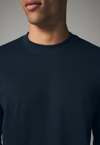 Marineblaues Langarm-T-Shirt aus weicher Baumwolle, mit Rundhalsausschnitt und gerippten Details am Kragen, glatte Textur und figurschmeichelnde Passform.