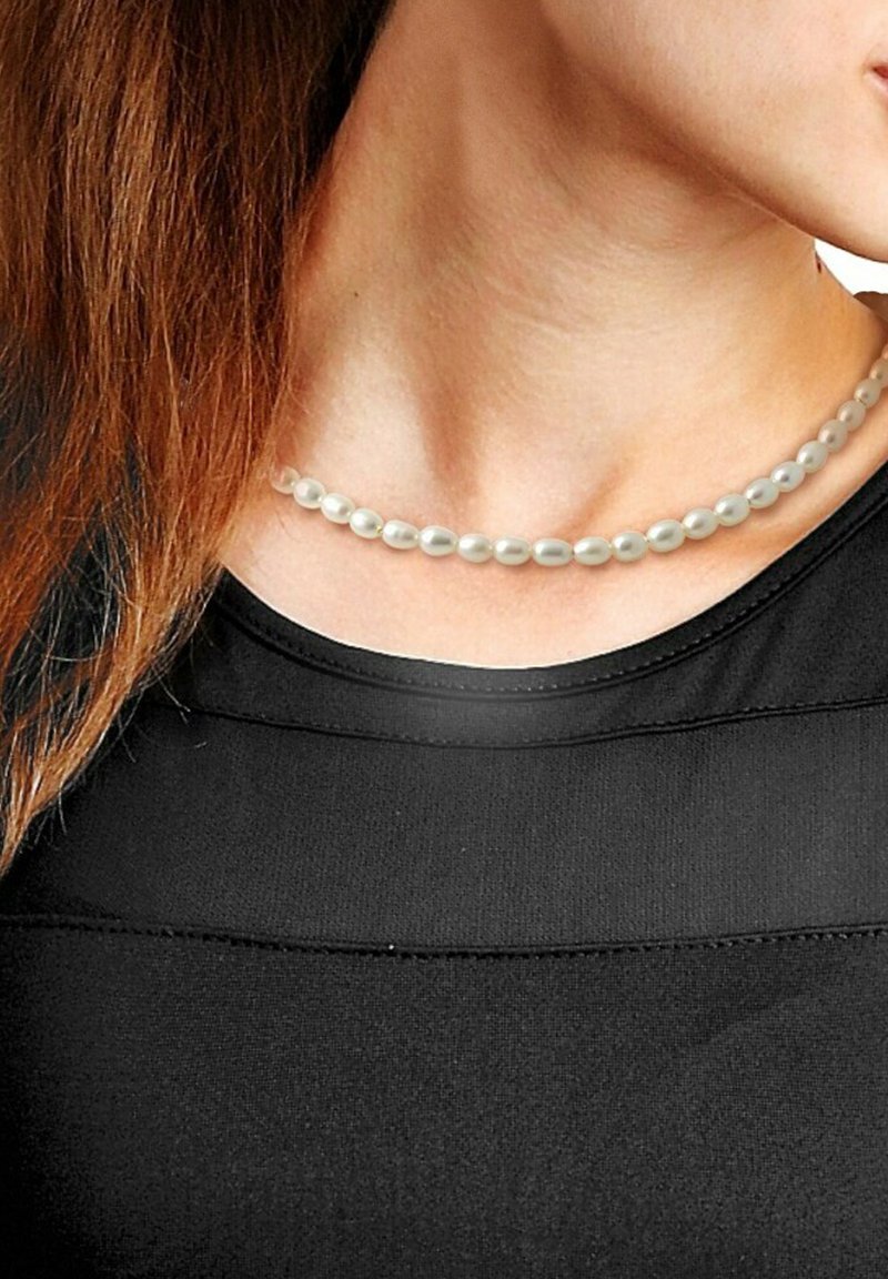 Collier en perles blanches avec des perles ovales, reposant sur un décolleté, associé à un haut noir ajusté avec des coutures horizontales.