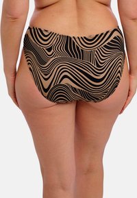 Vrouw in hoge bikinibroekjes met zwart en beige golvend gestreept patroon, van achteren gezien tegen een effen achtergrond.