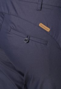 Navy blue pants featuring a button closure and a back pocket with a tan label, made of smooth, durable fabric.
