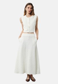 Valkoinen teksturoitu kaksiosainen asu, jossa on hihaton lyhyt toppi nappisuljennalla ja siihen sopiva polvipituinen hame, jossa on taskut.