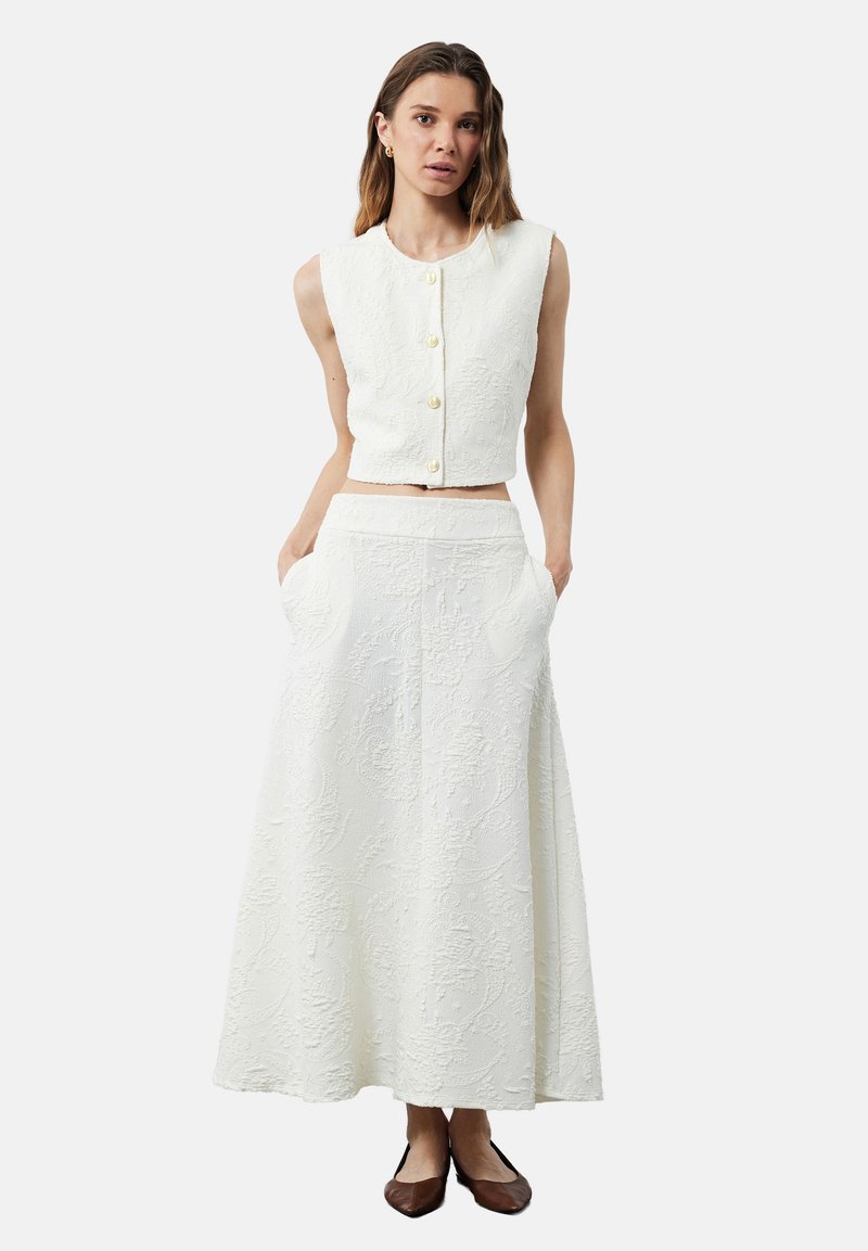 Valkoinen teksturoitu kaksiosainen asu, jossa on hihaton lyhyt toppi nappisuljennalla ja siihen sopiva polvipituinen hame, jossa on taskut.