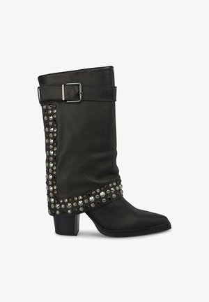 Botte cheville en cuir noir avec un bout pointu, ornée de clous métalliques sur le côté et d'une sangle avec une boucle en haut.