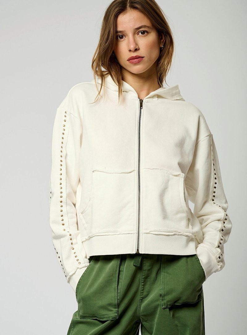 Sudadera con cremallera en color blanco roto, con capucha con cordón, dos bolsillos frontales y tachuelas decorativas a lo largo de las mangas. Material de algodón texturizado.