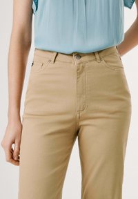 Beige bomullsblandningbyxor med hög midja, framfickor och lite stretch. Har en dragkedja och knappstängning.
