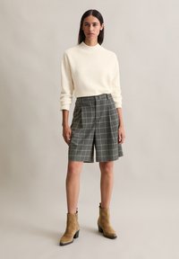 Crème, gebreide trui met hoge hals. Grijs geruite shorts met plooien, gecombineerd met tan enkelboots met een blokhak.