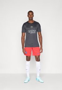 Sort sportstrøje med Qatar Airways-logo, parret med røde shorts med et blåt emblem. Hvide sokker og lyseblå fodboldsko fuldender outfittet.