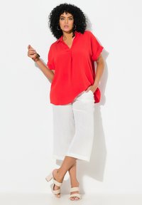Blouse rouge à manches courtes avec col, associée à un pantalon large blanc et des sandales à talons blocs nude. Comprend un tissu fluide et une coupe décontractée.