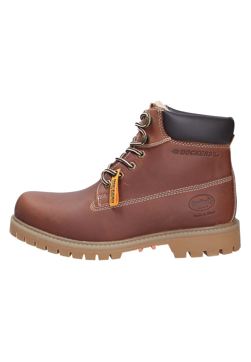 Bottines en cuir marron avec œillets métalliques, semelle extérieure robuste et col rembourré. Comprend une étiquette de marque jaune et des coutures contrastées.