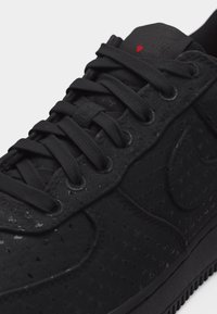 Μαύρο αθλητικό παπούτσι με μαύρα κορδόνια, διάτρητο μοτίβο αστεριού στο πάνω μέρος και μια μικρή κόκκινη καρδιά στη γλώσσα.