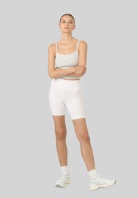 Szary skrócony top i białe spodenki rowerowe z wysokim stanem; dopasowany krój z elastycznego materiału; gładkie, bez wzorów; połączone z jasnymi sneakersami.